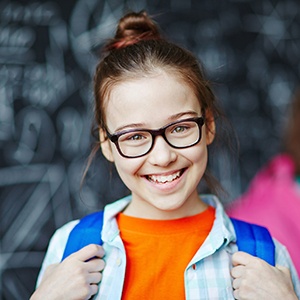 Young girl sporting spectacles and backpack smiling
