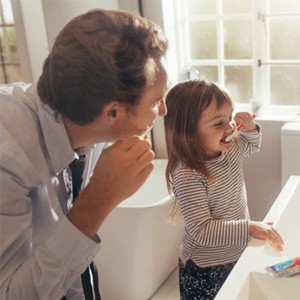 Father and daughter brushing their teeth together in bathroom