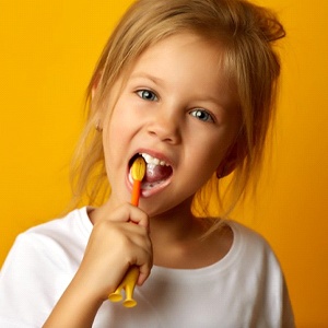 little girl brushing her teeth against a yellow-orange background