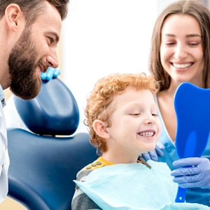 little boy sitting in dental chair and smiling at hand mirror