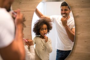 Father and daughter brushing their teeth in front of a mirror 