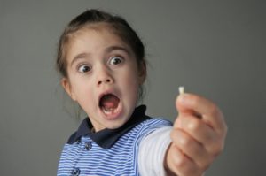 Little girl holding tooth is shocked at losing baby teeth