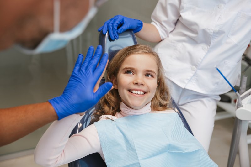 Young girl giving dentist high-five in treatment chair