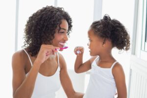Woman and little girl in white shirts brushing their teeth together