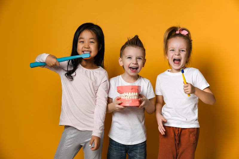 three young kids smiling with dental hygiene tools