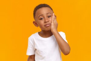 Little boy holding hand to jaw in pain with orange background